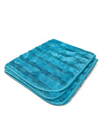 A folded turquoise blue striped bath mat made of soft terry cloth, shown on a plain white background.